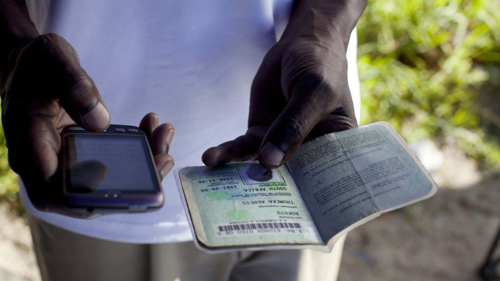 A bank employee selling accounts on the street uses a mobile phone to check an identity document, outside of Cape Town, South Africa.