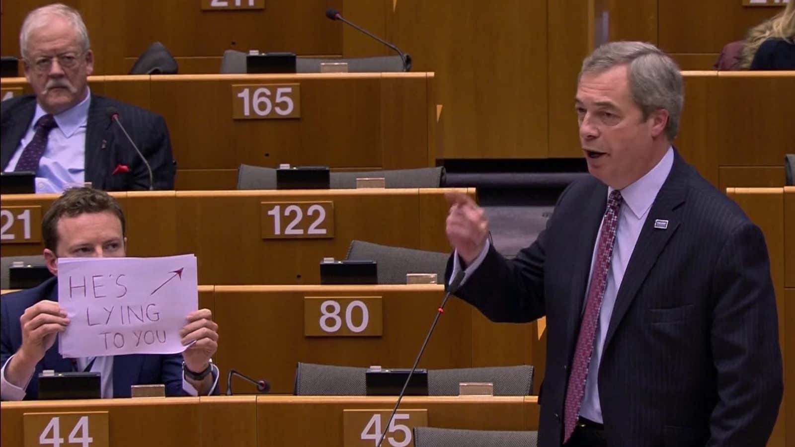 In this image made from video, Labour MEP Seb Dance, left, holds up a sign as UK Independence Party MEP Nigel Farage addresses the European…