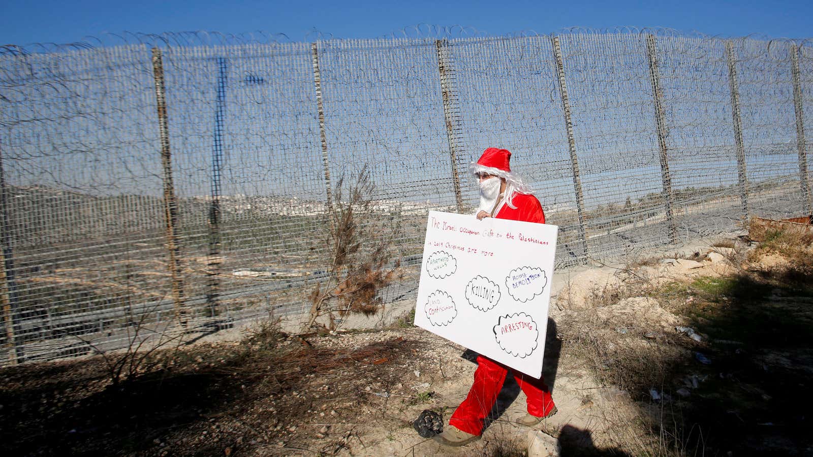 A Palestinian demonstrator dressed as Santa Claus the Israeli barrier with the West Bank.