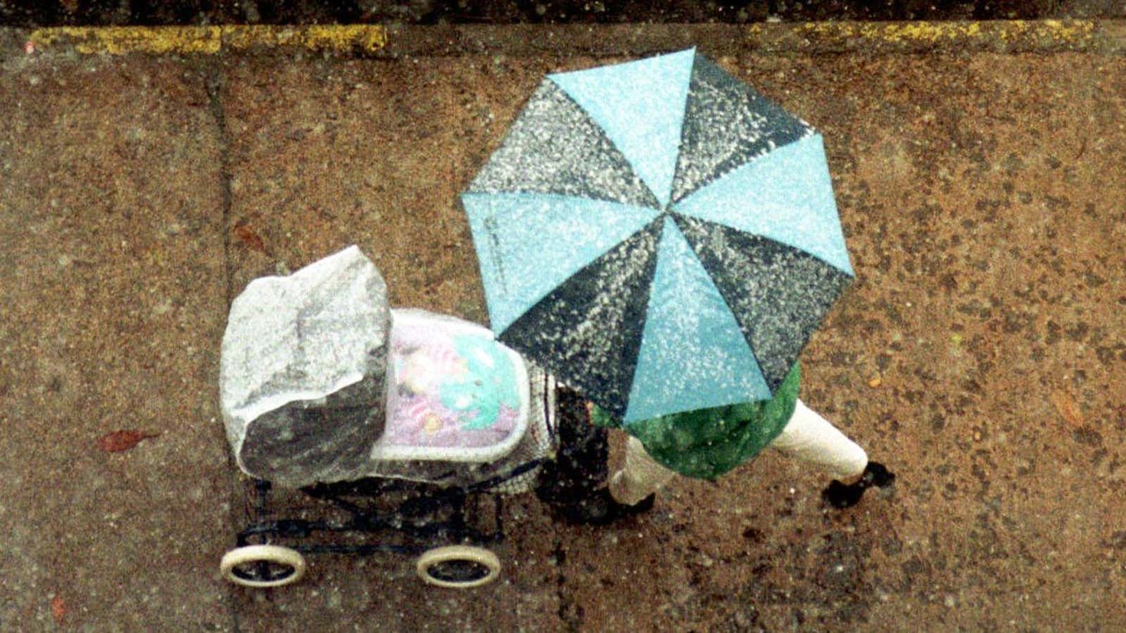 A woman, sheltered by an umbrella, passes a snow-covered car , while taking a stroll with a baby carriage in downtown Erfurt, Germany, Monday December…