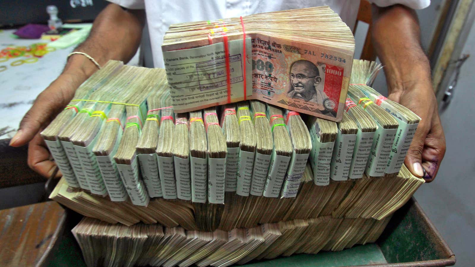 An employee poses with the bundles of Indian rupee notes inside a bank in Agartala, the capital of India’s northeastern state of Tripura August 22,…