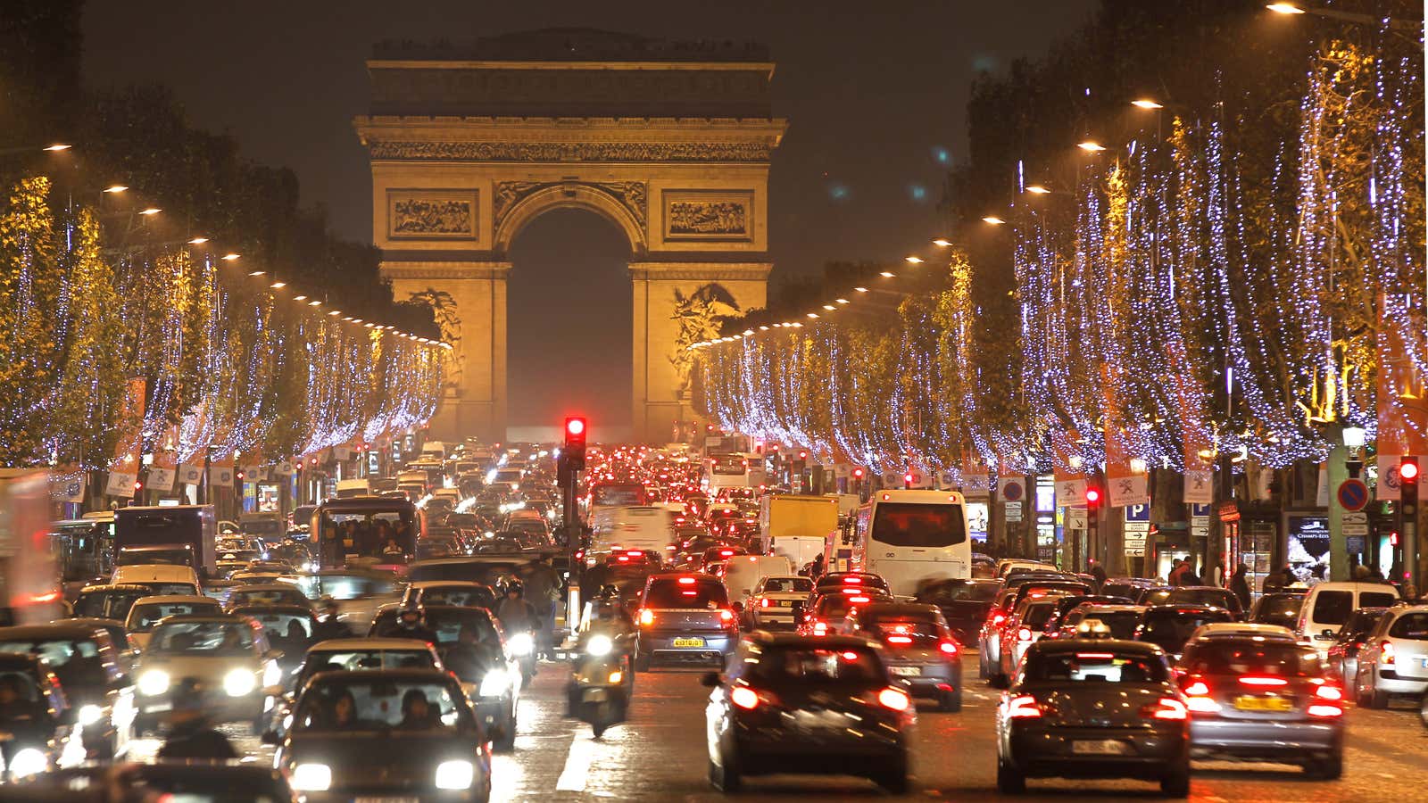 Holiday lights hang from trees to illuminate Champs Elysees in Paris as rush hour traffic fills the avenue leading up to the Arc de Triomphe…