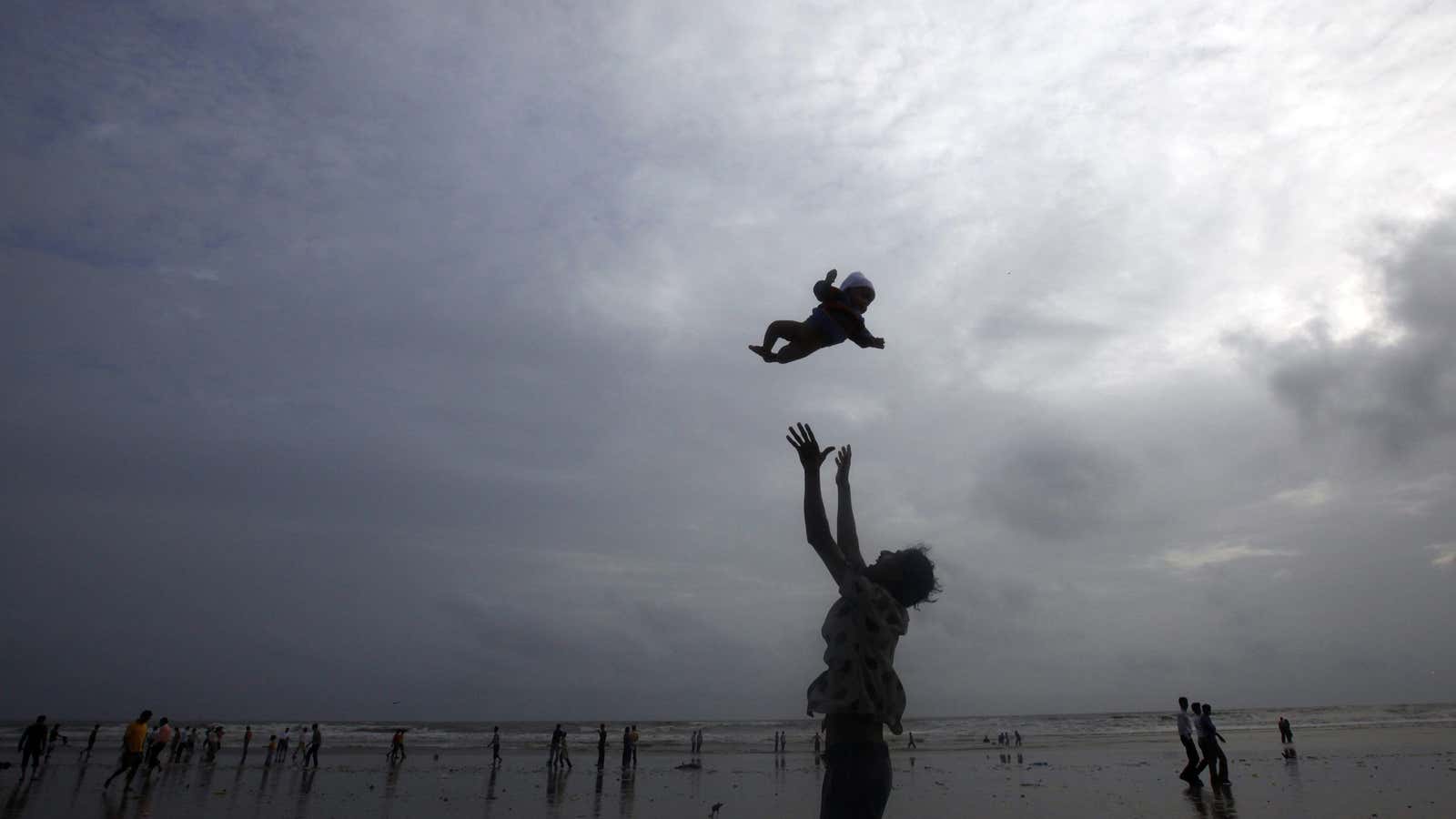 A man plays with his child against the backdrop of monsoon clouds on a beach in Mumbai July 23, 2010.