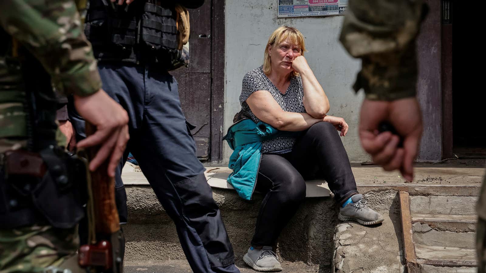 A local resident sits near her apartment building, as police officers stand, as Russia’s attack on Ukraine continues, in Lysychansk.