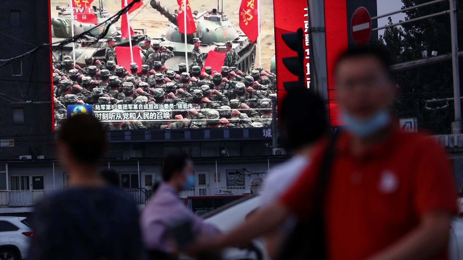 Pedestrians walk past a screen showing footage of Chinese People&#39;s Liberation Army (PLA) soldiers during an evening news programme, in Beijing.
