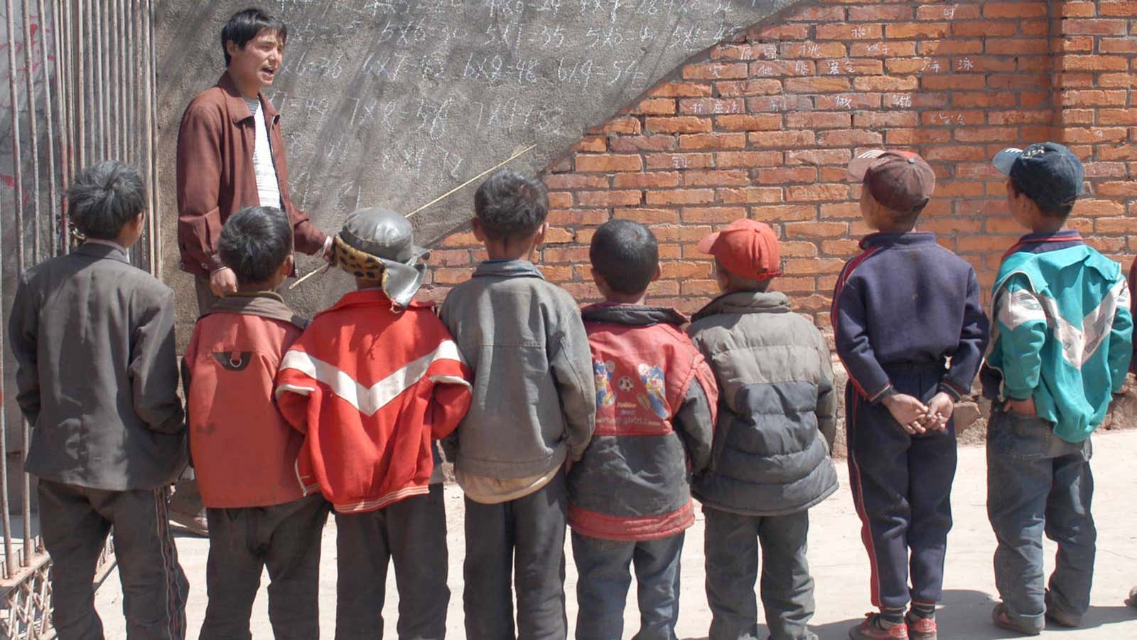 A teacher uses a wall as a makeshift blackboard. China has imparted strong math skills to a largely poor population by adding more classes.