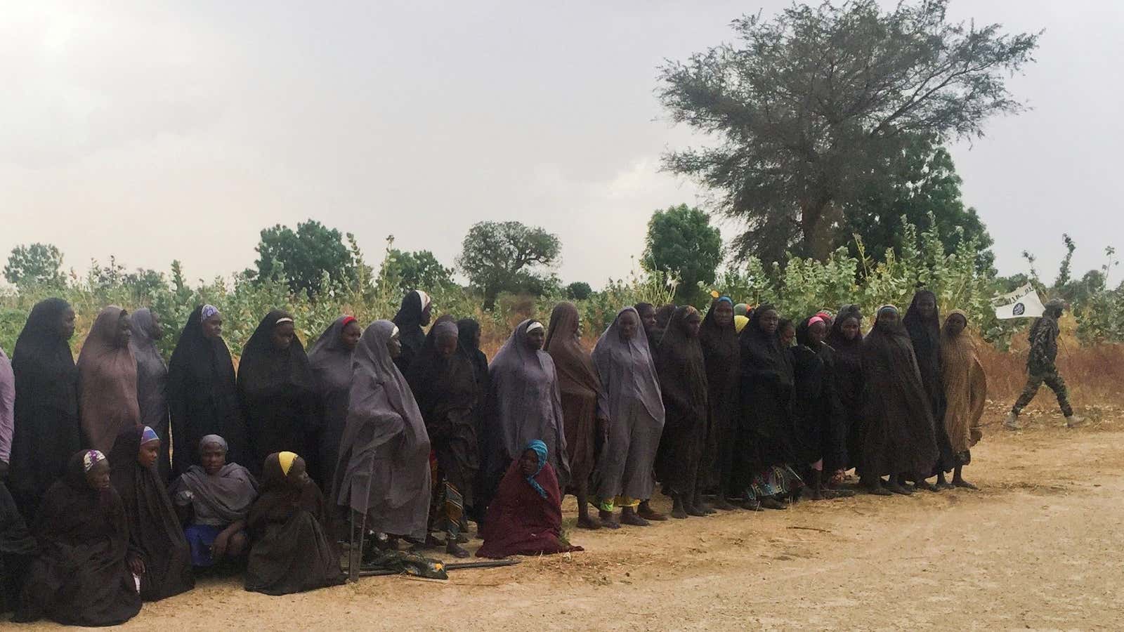 A man carrying a Boko Haram flag walks past a group of 82 Chibok girls, who were held captive for three years by Islamist militants. May 6, 2017.