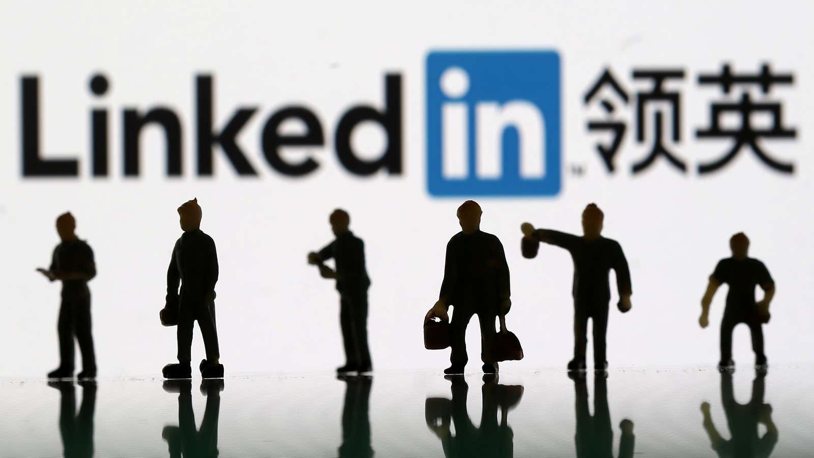 Small toy figurines of people are arranged in front of a logo for LinkedIn China.