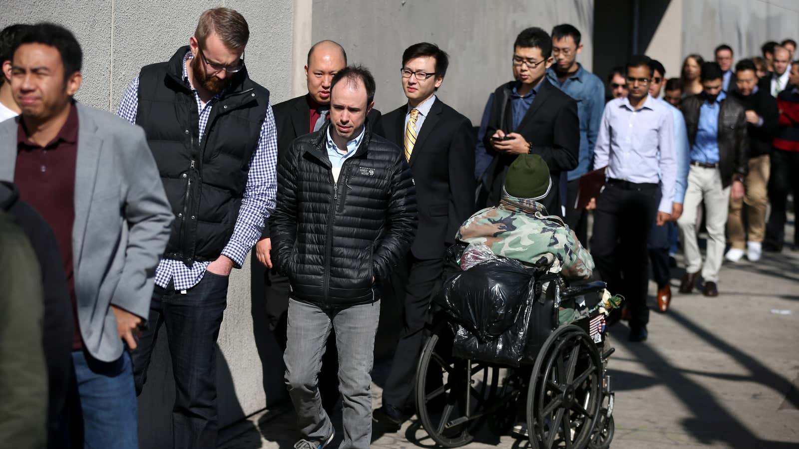 People pass a man begging as they wait in line to attend TechFair LA, a technology job fair, in Los Angeles.