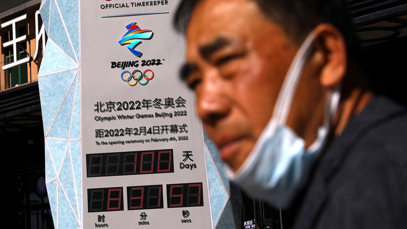 A man stands in front of a Beijing Olympics 2022 sign.