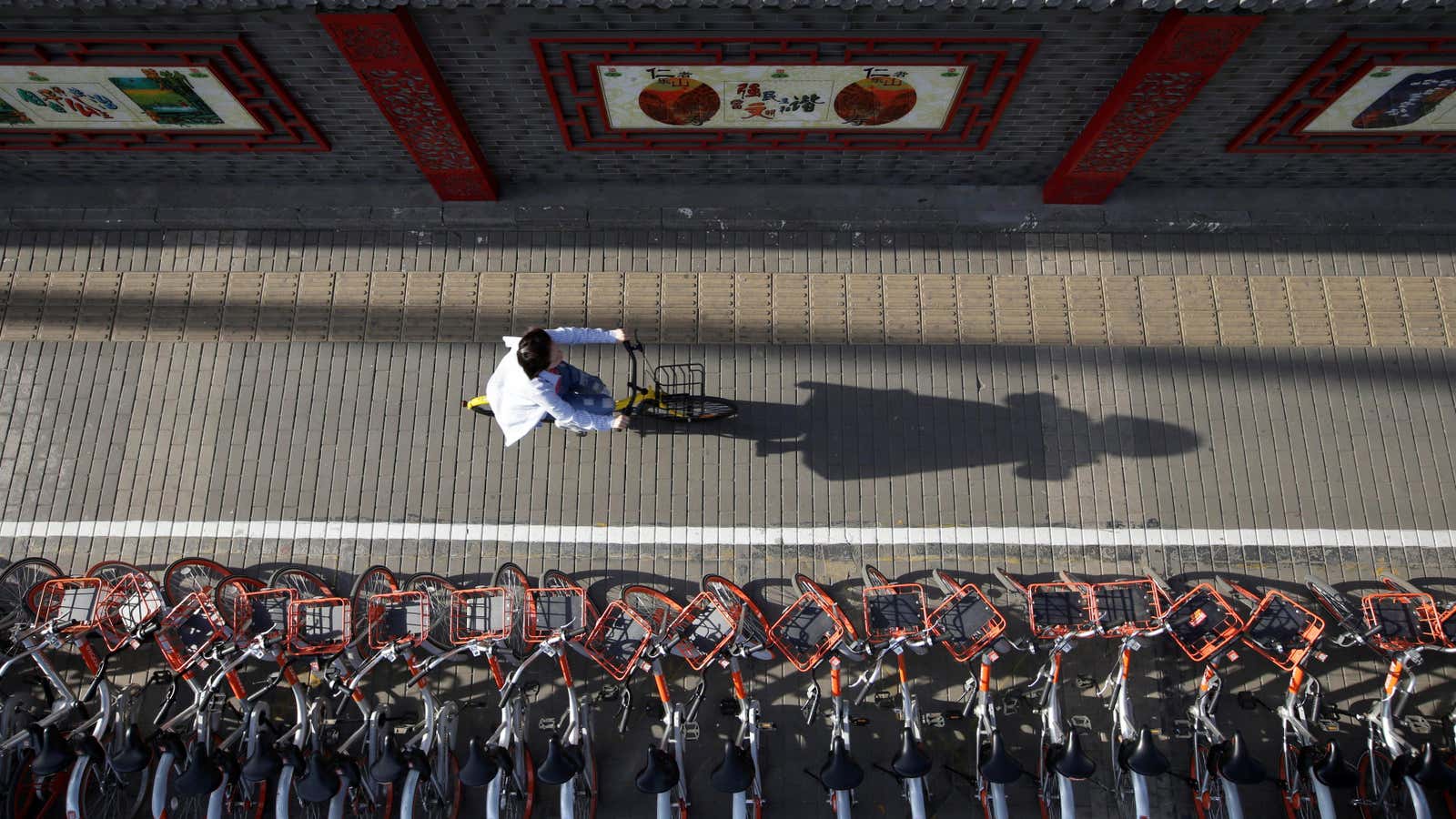 A woman rides an Ofo&#39;s shared bike past Mobike&#39;s shared bikes in Beijing.