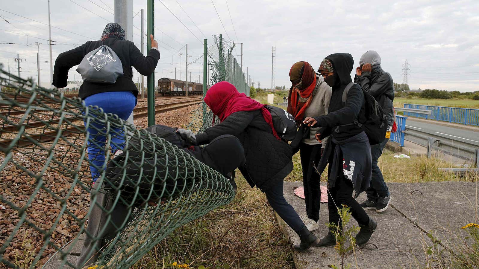 Migrants make their way across a fence near near train tracks as they attempt to access the Channel Tunnel in Frethun, near Calais, France, July…