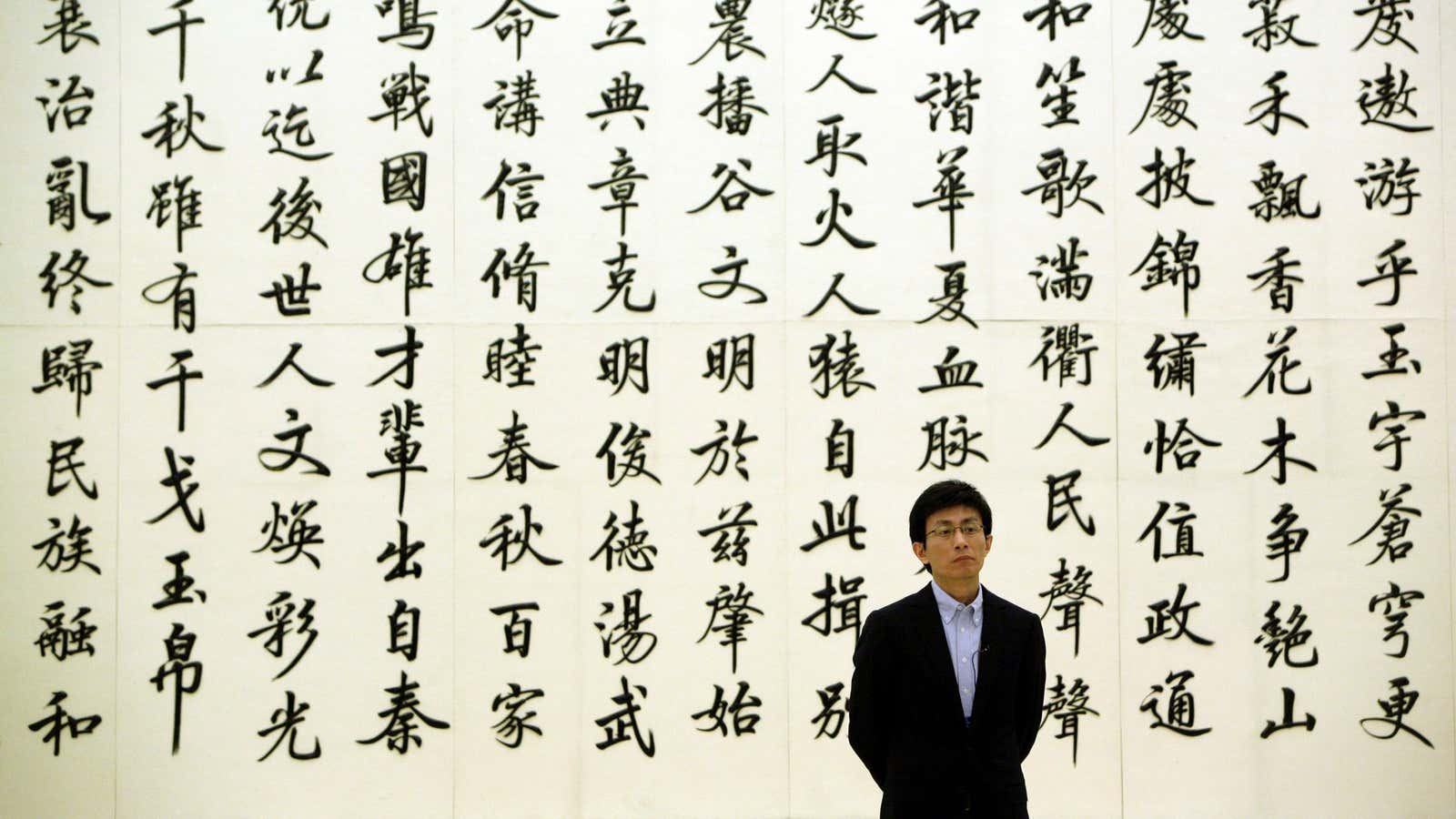 A man stands in front of a marble wall engraved with Chinese calligraphy poetry, in the Great Hall of the People, in Beijing.