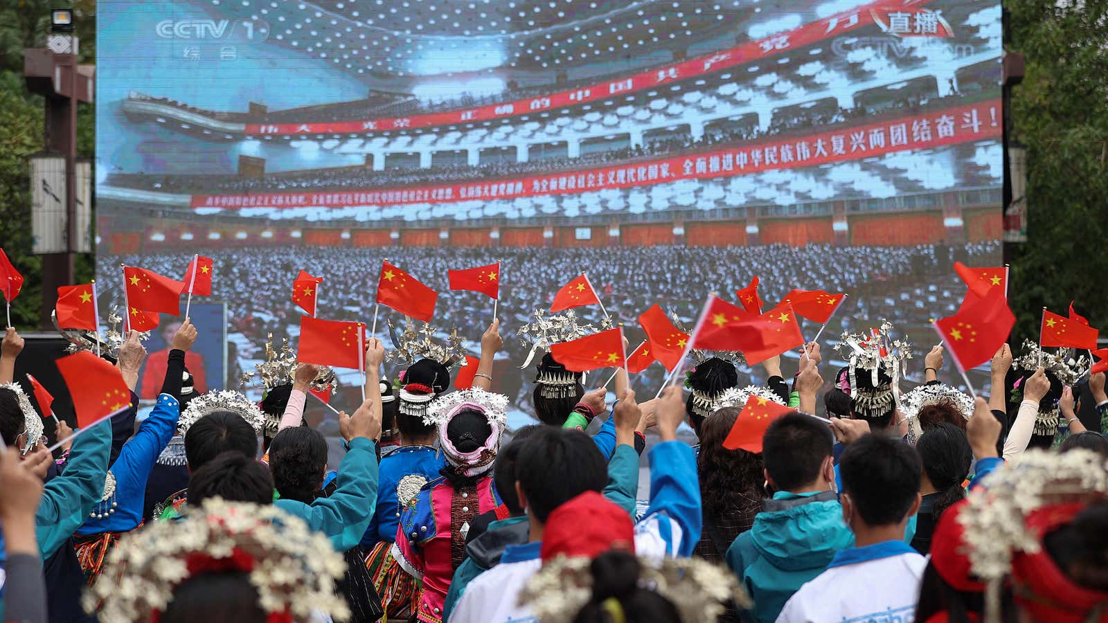 Ethnic minority members wave national flags as they watch the opening session of the 20th Chinese Communist Party Congress on a screen in Danzhai, in China&#39;s southwestern Guizhou province on October 16, 2022.
