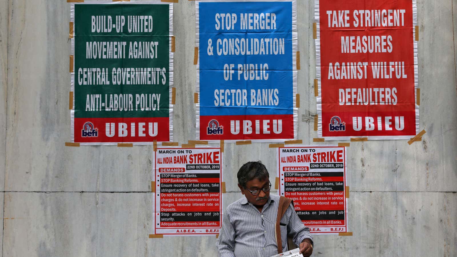 A bank employee reads a newspaper in front of a United Bank of India branch building during a day-long strike against mergers of several state-run…