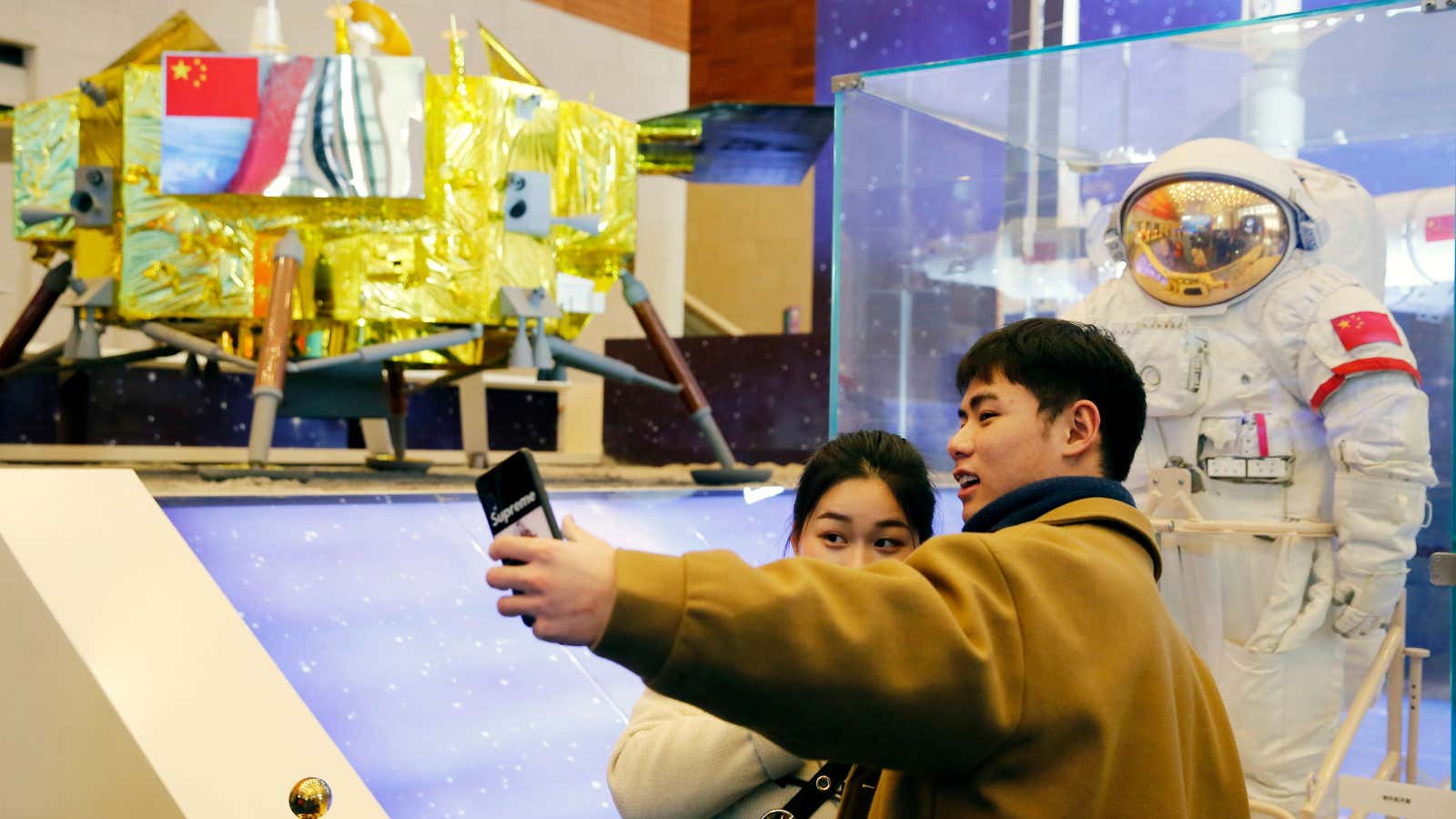 Chinese visitors take photos beside a Chinese space suit and a model of the Chang’e-3 lunar probe.