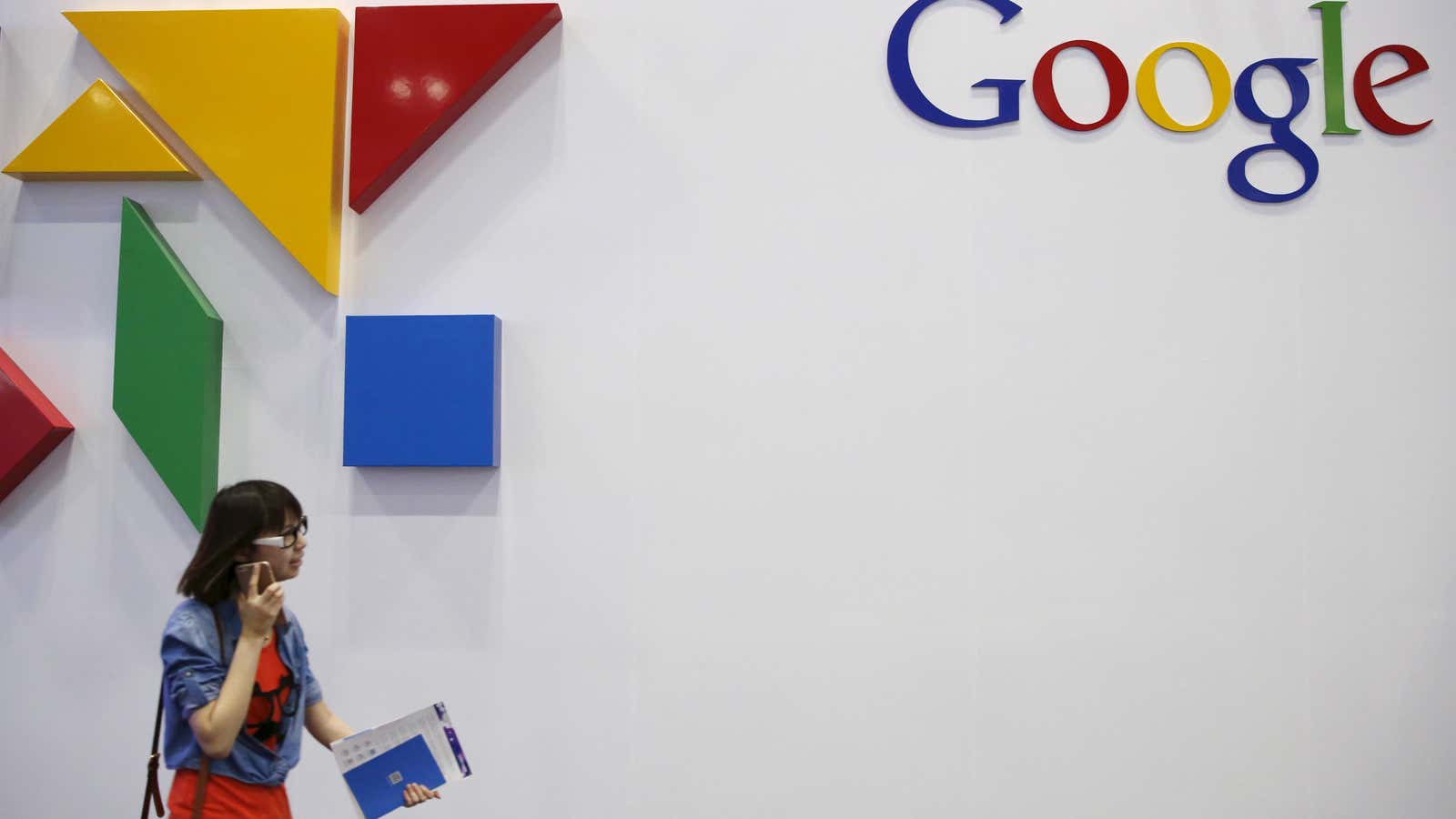 A woman walks past a logo of Google.