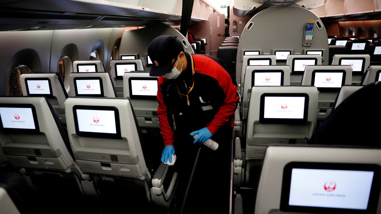 FILE PHOTO: A staff member of Japan Airlines wearing a protective face mask and gloves cleans the cabin of a plane which performed a domestic…