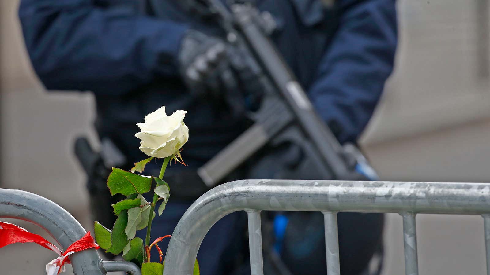 A white rose is attached to a barrier as a French policeman with an automatic weapon secures the area near the Bataclan concert hall the…