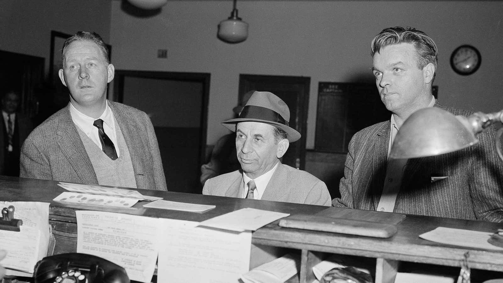 Meyer Lansky is booked by New York City detectives in 1958 to be questioned about a gangland slaying.