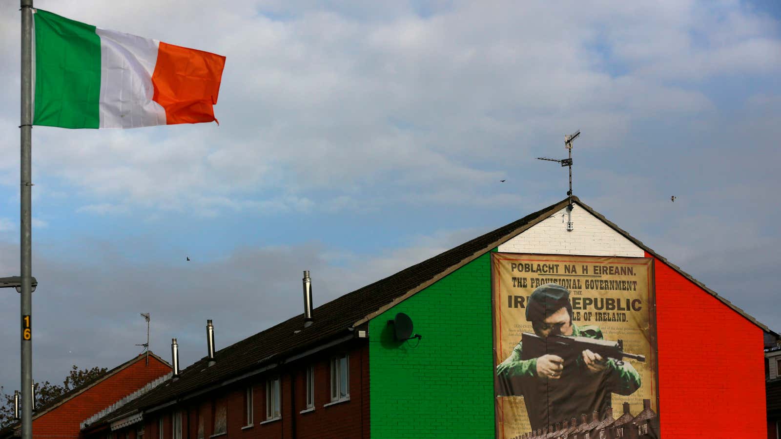 An Irish flag waves beside a mural depicting an IRA gunman north of Belfast, the capital of Northern Ireland.