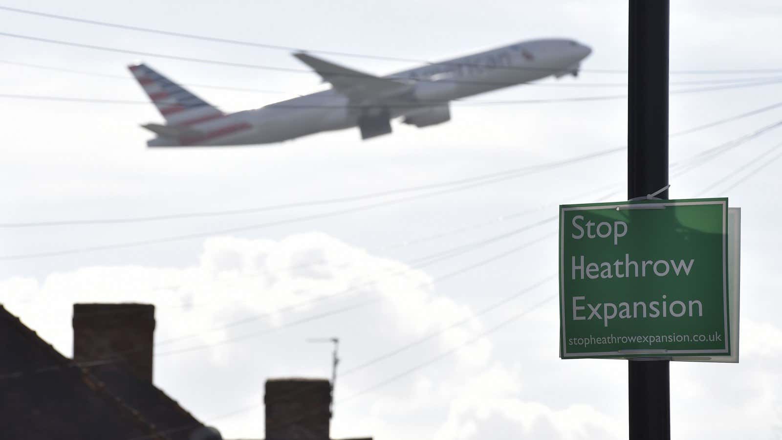 A passenger aircraft is seen taking off behind a campaign poster attached to a street lamp near Heathrow airport, west London, March 5, 2015. Business…