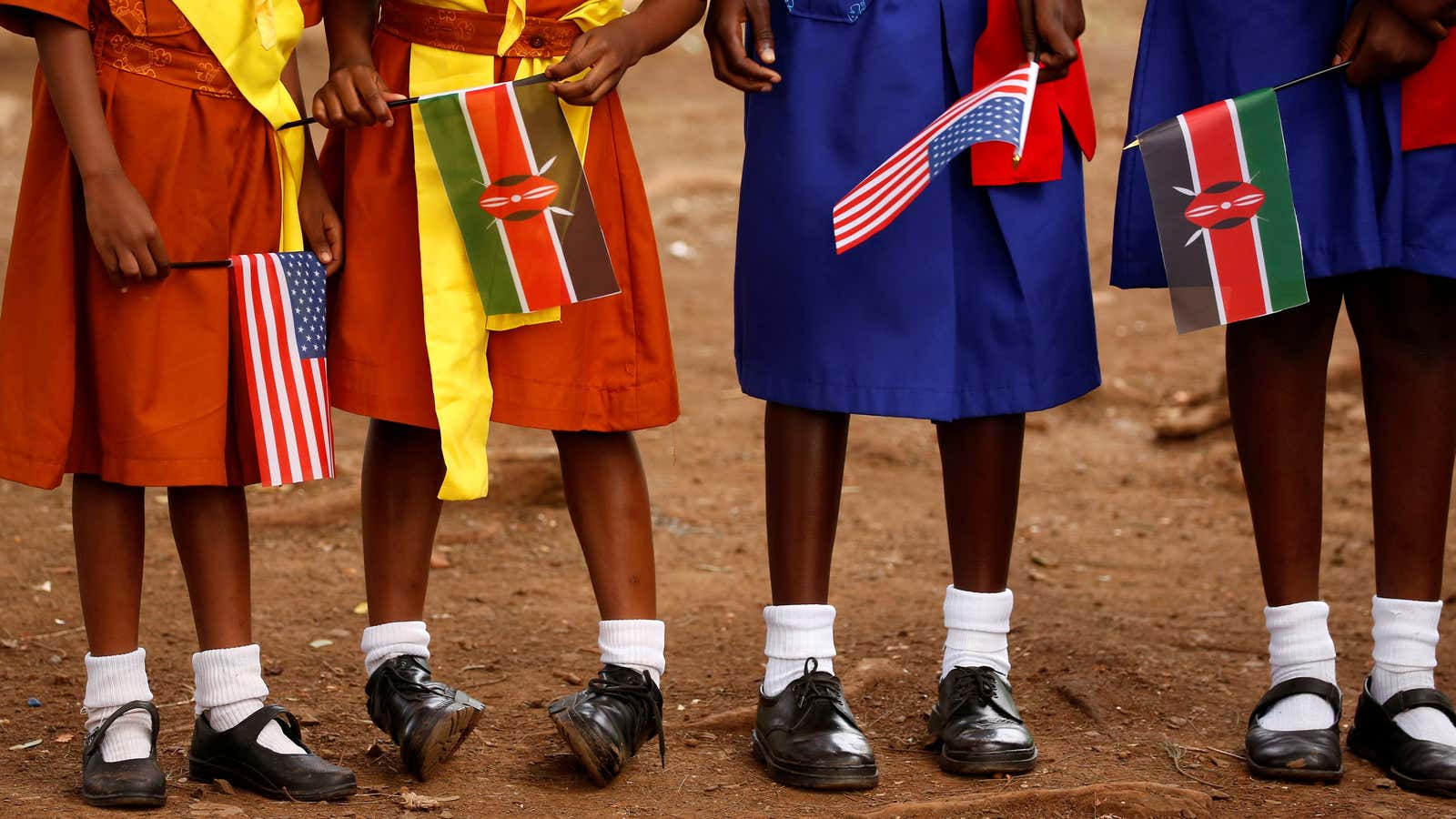 Young girls with U.S. and Kenya flags wait to greet U.S. Ambassador to Kenya Robert Godec as he visits a President’s Emergency Plan for AIDS…