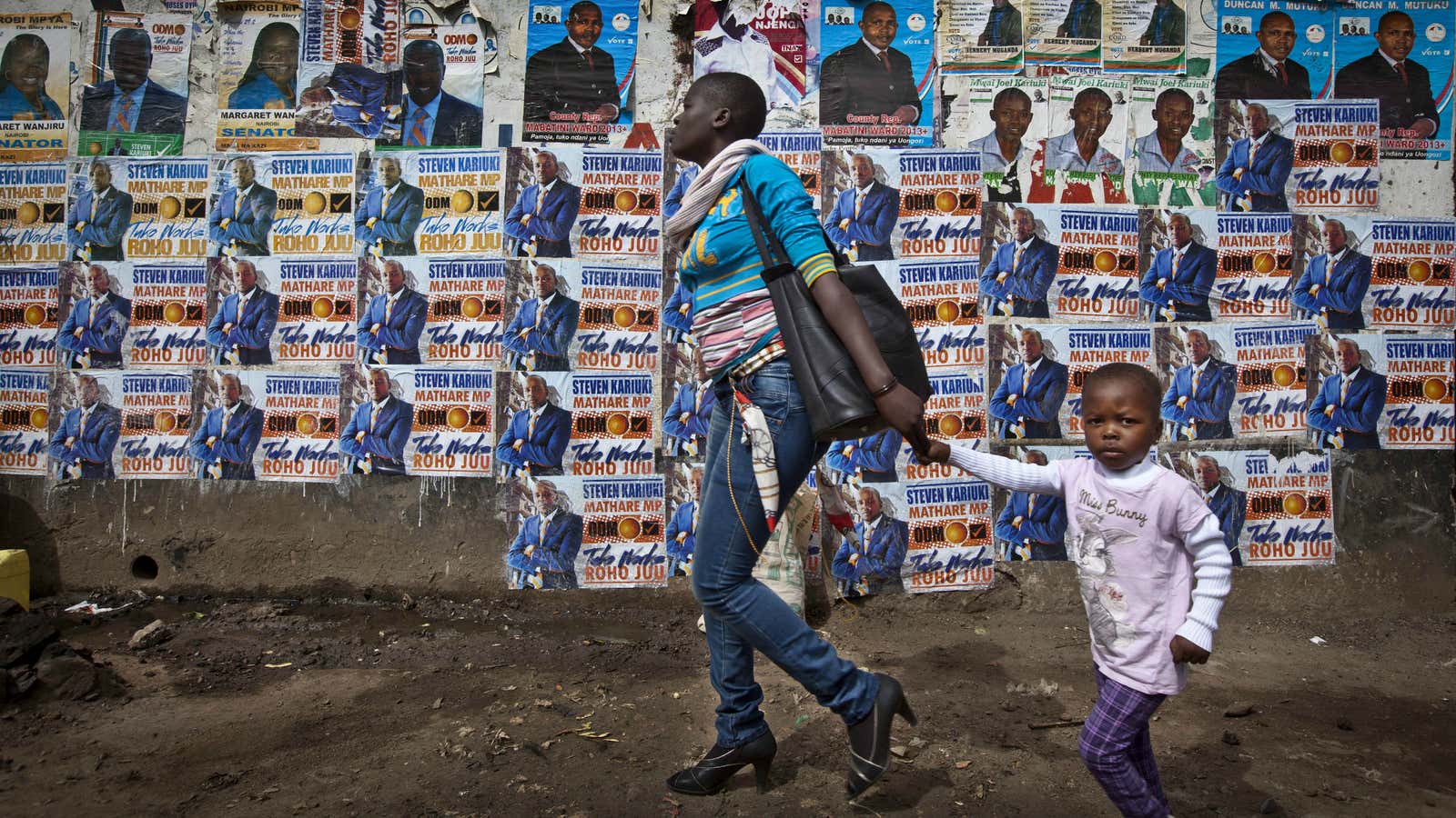 A mother and her child walk past a wall plastered with election campaigning posters in the Mathare slum of Nairobi.