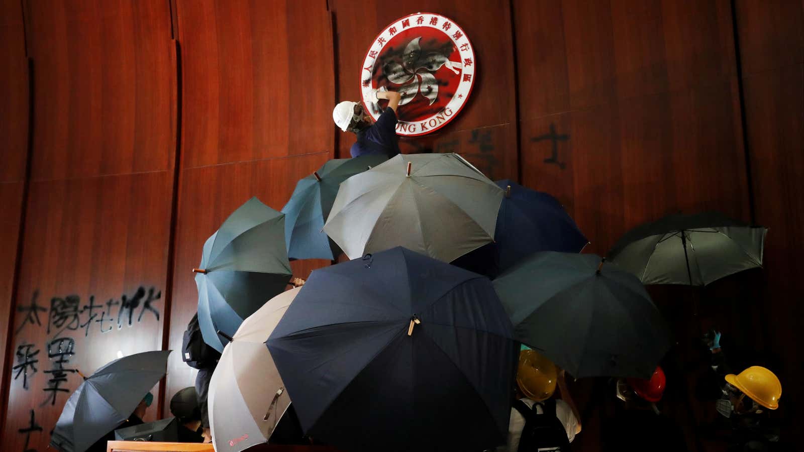 A person sprays paint over Hong Kong’s coats of arms inside a chamber after protesters broke into the Legislative Council building during the anniversary of…