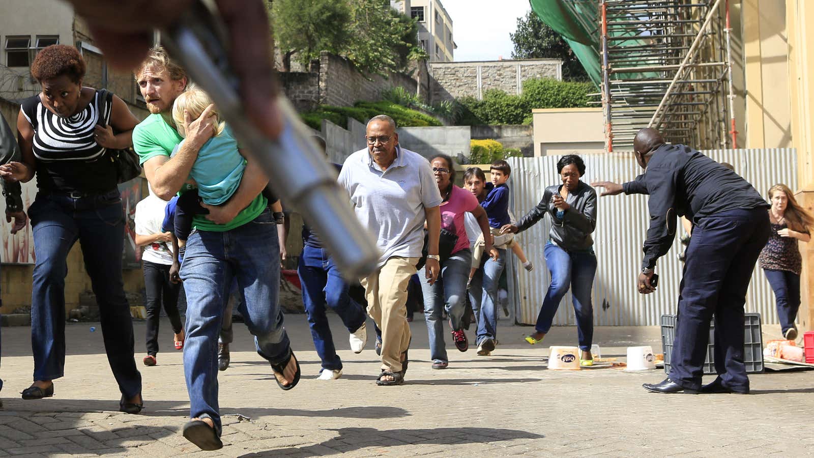 A policeman’s gun provides cover as people flee the mall.