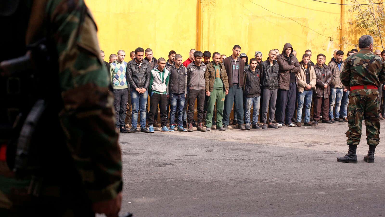 Members of Syria’s government military police stand guard as men who were evacuated from the eastern districts of Aleppo are prepared to begin military service.