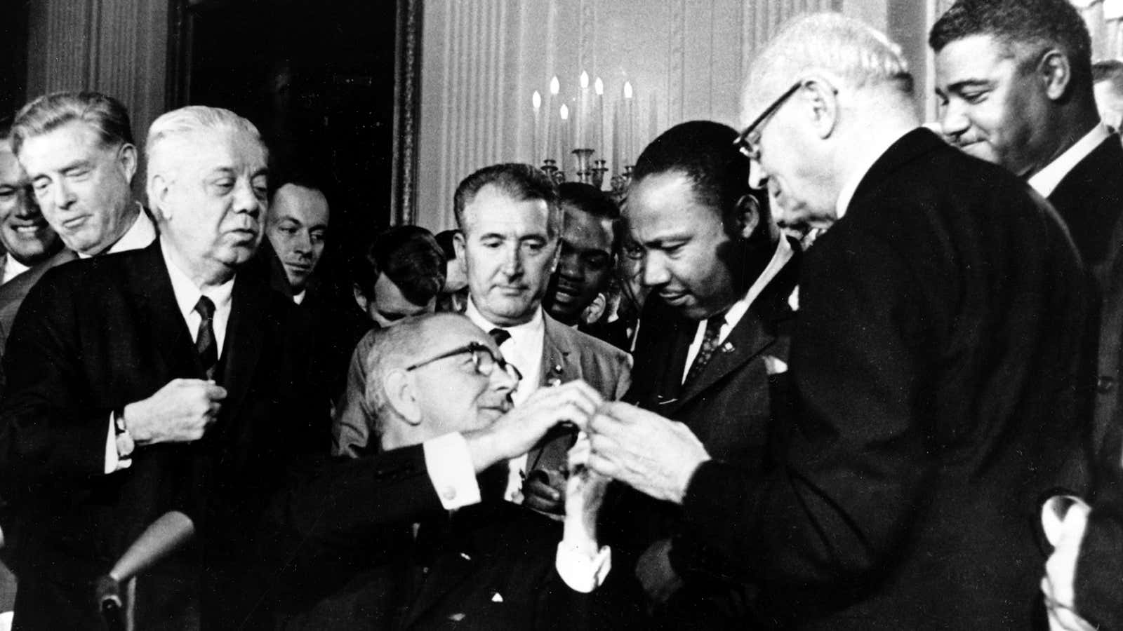 President Johnson shakes hands with Martin Luther King Jr. after signing the act.