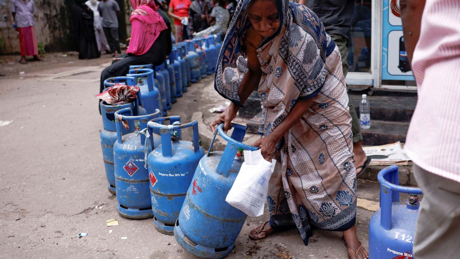 A woman moves a gas tank as she stands in line to buy another tank near a distributor, amid the country’s economic crisis, in Colombo, Sri Lanka.