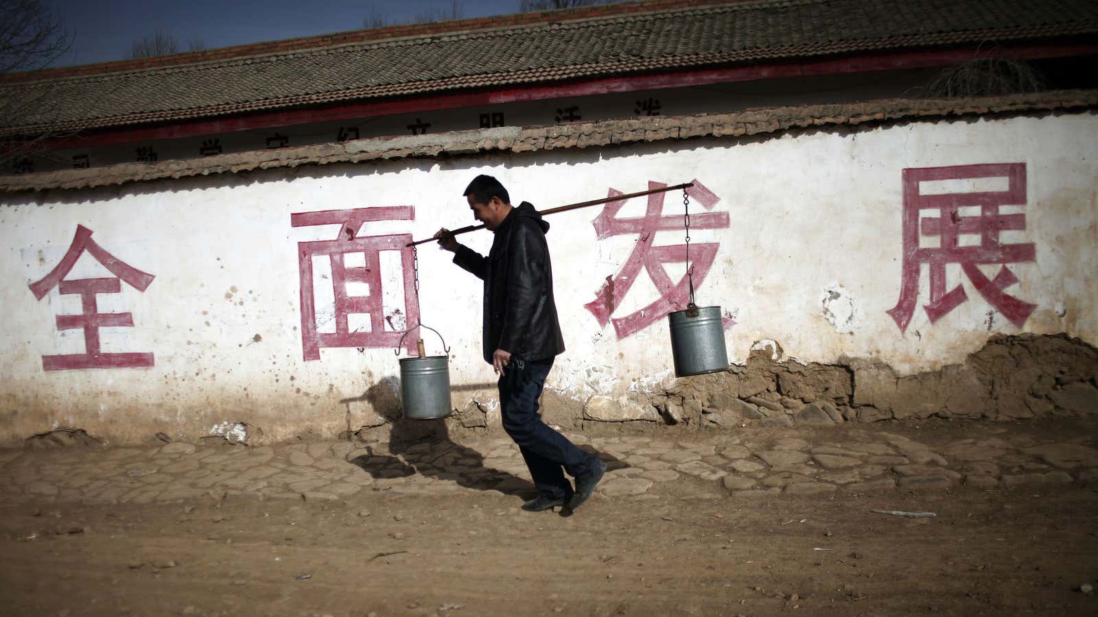 A villager walks in Gansu province walks in front of a wall with the words, “Comprehensive development.”