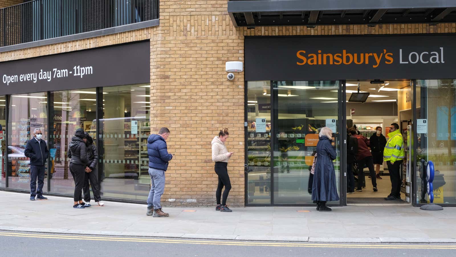 People wait in line to shop at a Sainbury’s Local in London.