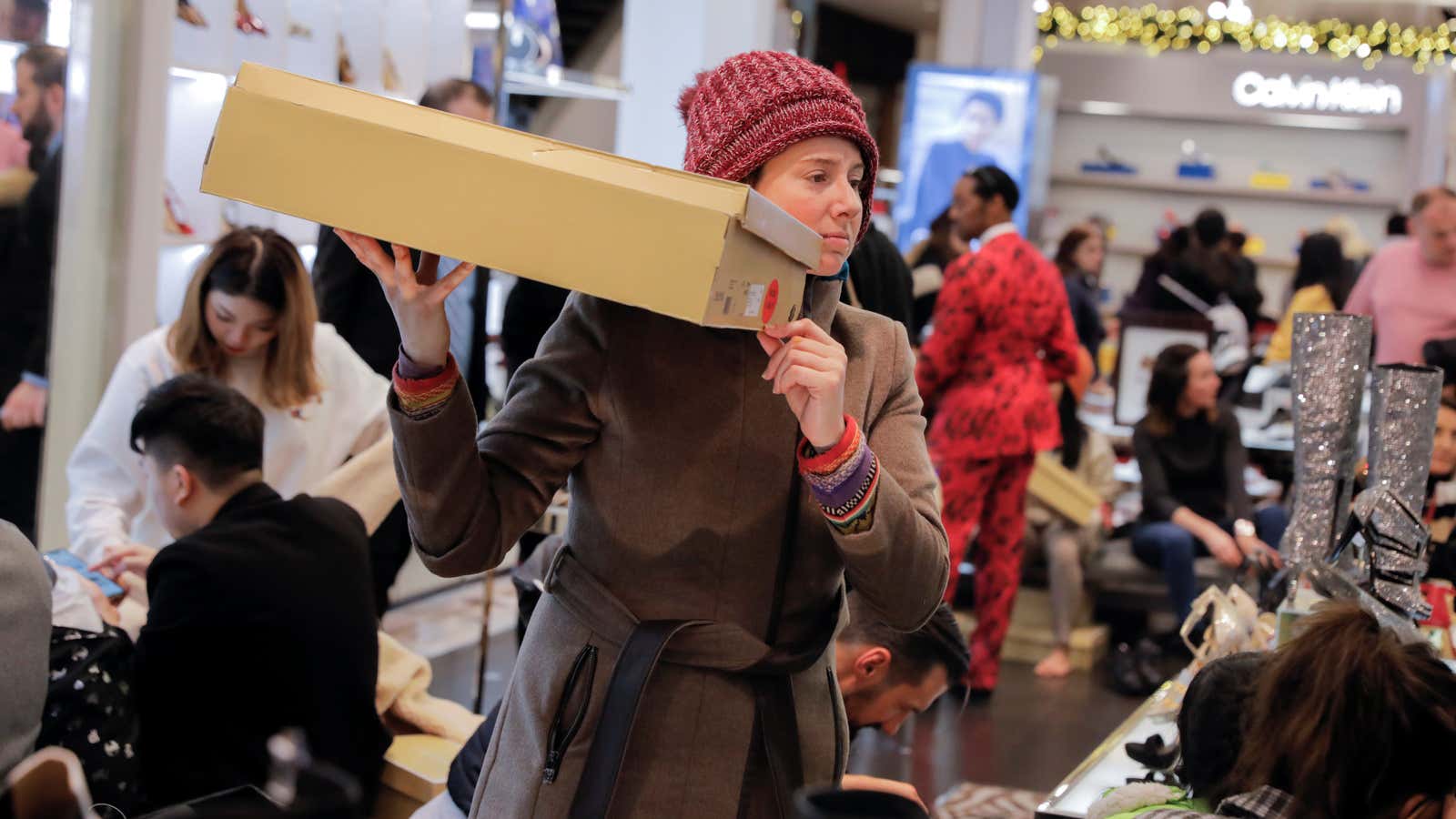 A woman holds a box aloft amid a sea of holiday shoppers at a Macy’s department store.