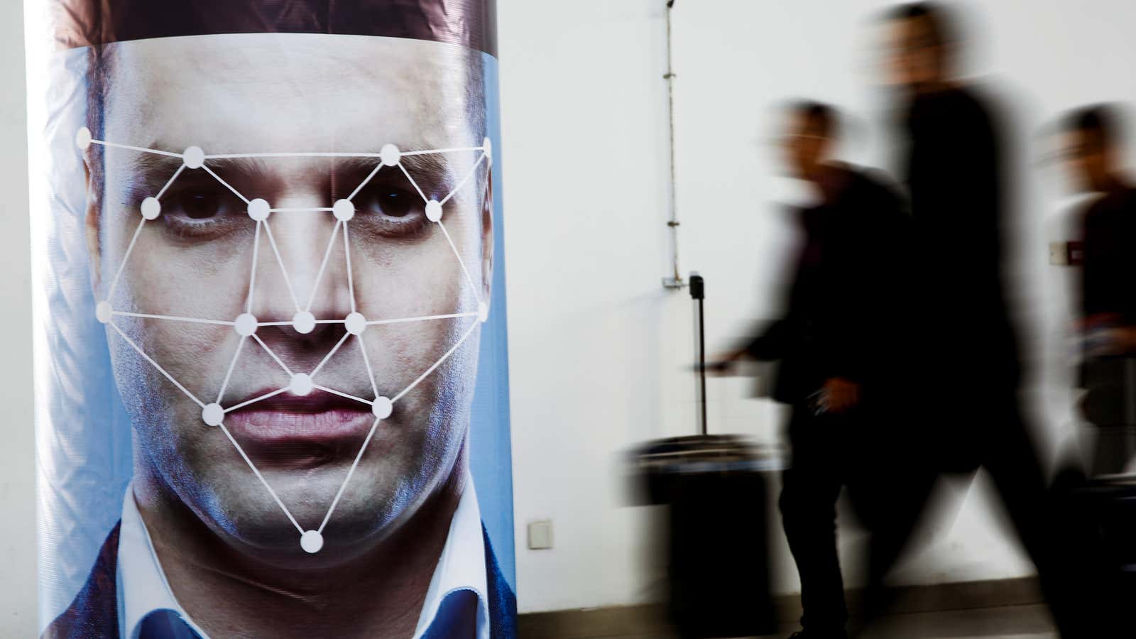 People walk past a poster simulating facial recognition software at the Security China 2018 exhibition on public safety and security in Beijing, China October 24,…