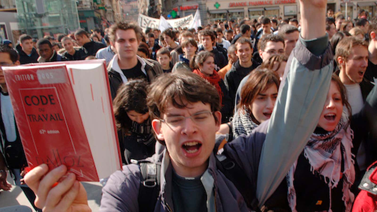 A young college student center brandishing the French work code during a protest against a jobs plan, known as the First Job Contract or CPE in Lyon, France Tuesday, March 21, 2006. Escalating protests in France center on a new job contract that allows employers to fire young workers within their first two years without giving a reason. This is designed to give employers flexibility, thereby encouraging them to hire more young people. For several days, tens of thousands of French students marched, chanted and whistled in renewed nationwide protests against a new labor law, as the government tried to maintain a united front for this pivotal test of the country’s direction. (AP Photo/Patrick Gardin)