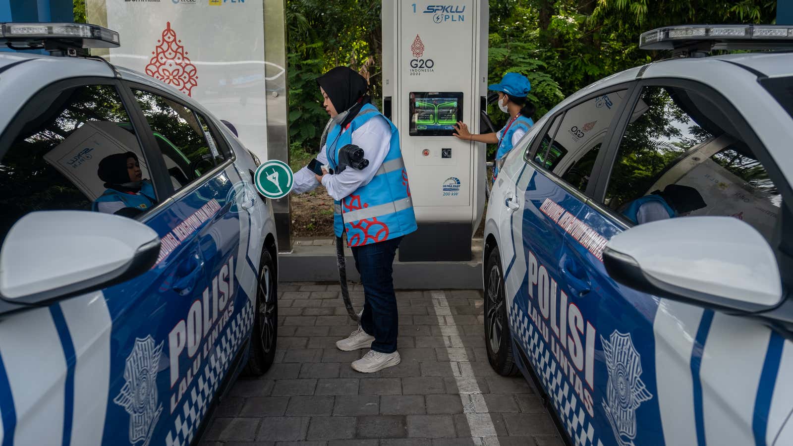 Two women charge electric police cars for the G20 Bali Summit at The Nusa Dua on November 13, 2022.