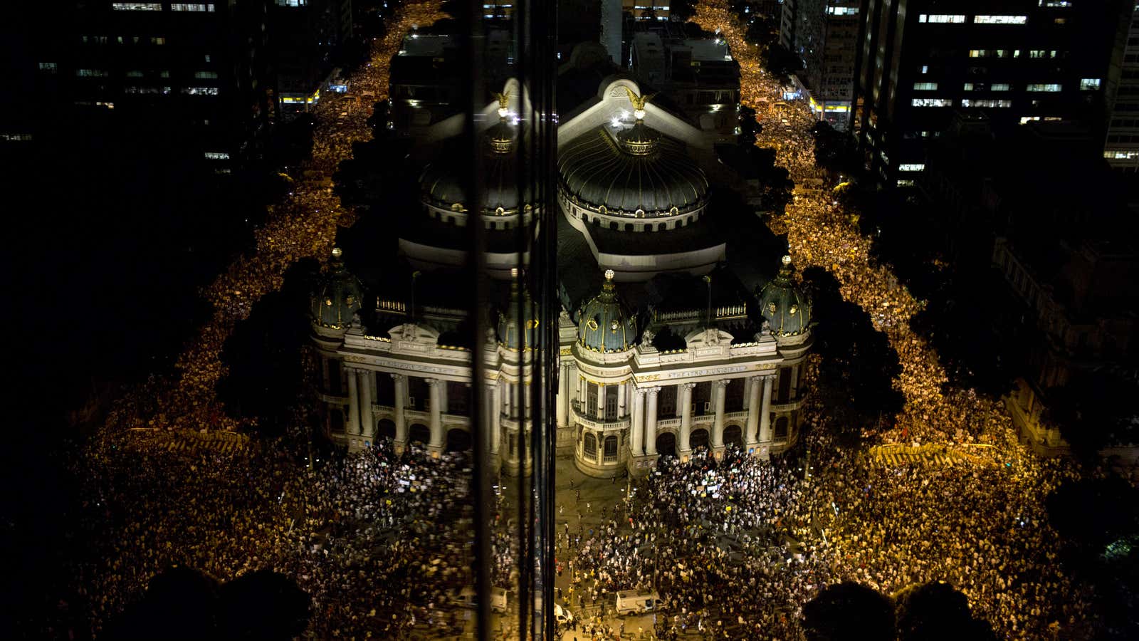 Protestors are reflected on the glass of a building, left, as they march in Rio de Janeiro.