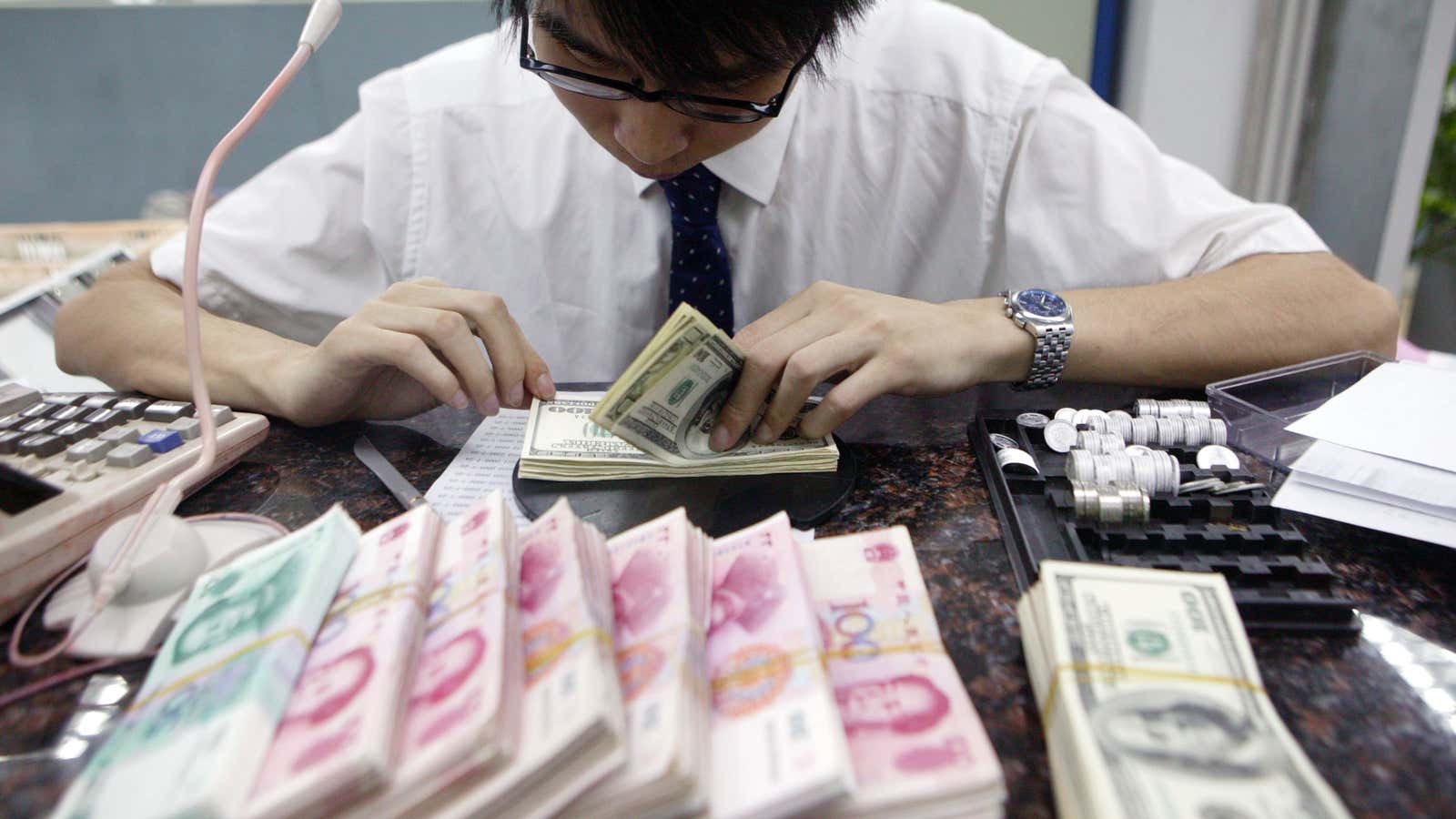 A clerk counts stacks of Chinese yuan and U.S. dollars at a bank in Shanghai, China.