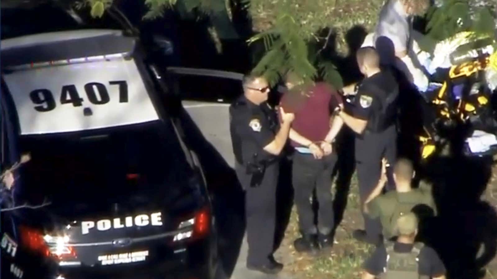 A man placed in handcuffs is led by police near Marjory Stoneman Douglas High School.