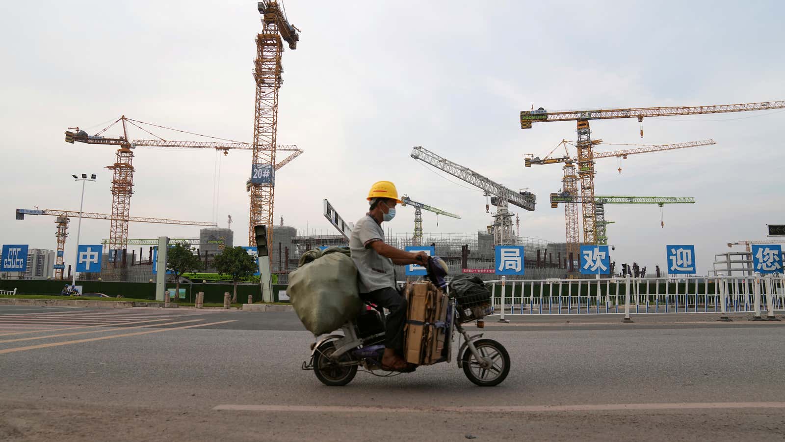 A man rides an electric bicycle past the construction site of Guangzhou Evergrande Soccer Stadium, a new stadium for Guangzhou FC developed by China Evergrande…