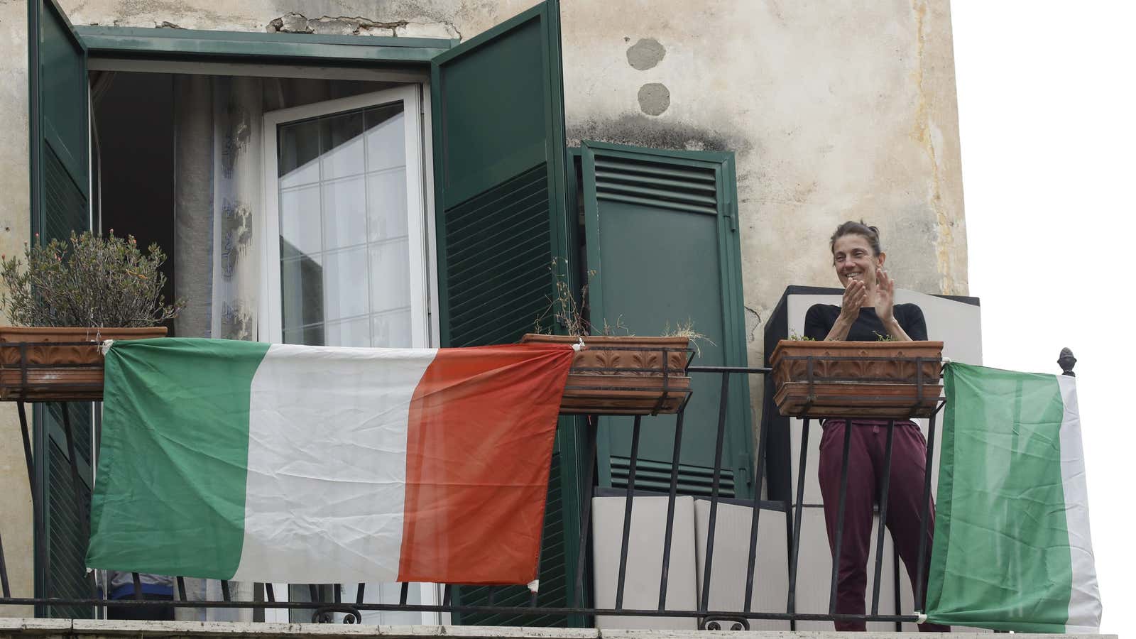 A woman applauds as she stands on her balcony adorned with the Italian flag, at the Garbatella neighborhood, in Rome, Saturday, March 14, 2020. The nationwide lockdown to slow coronavirus is still early days for much of Italy, but Italians are already showing signs of solidarity with flash mob calls circulating on social media for people to ”gather” on their balconies at certain hours, either to play music or to give each other a round of applause. For most people, the new coronavirus causes only mild or moderate symptoms. For some, it can cause more severe illness, especially in older adults and people with existing health problems. (AP Photo/Alessandra Tarantino)