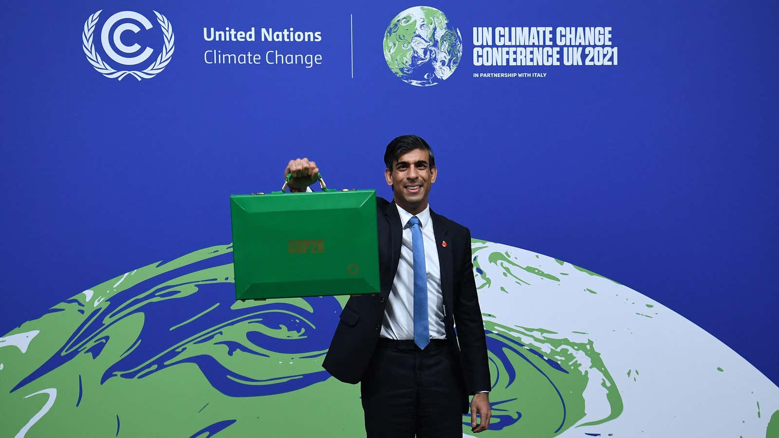 Britain’s Chancellor of the Exchequer Rishi Sunak holds up a green briefcase similar to the red Budget Box while standing in front of a sign…