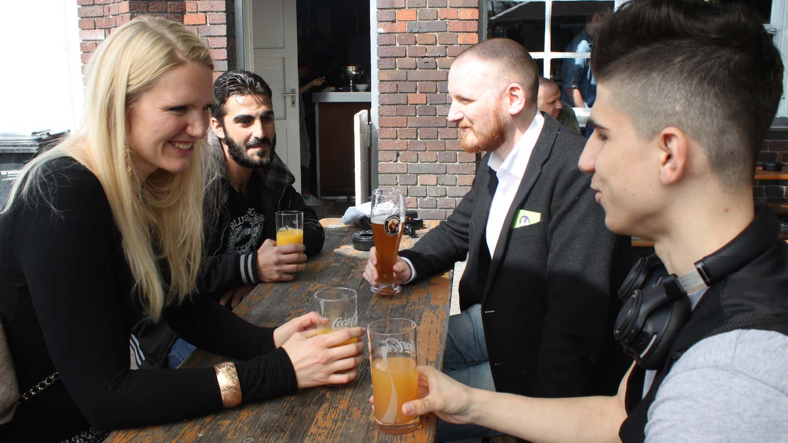 In this May 1, 2016 photo Cindy Spieker, Ahmed Haj Ali, Paul Spieker and Abdul Wahab, from left, sit around a table in Berlin. The…