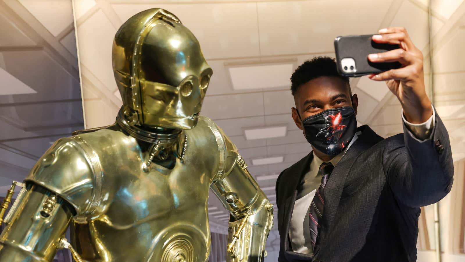 A fan takes a selfie next to a model of Star Wars character C-3PO.