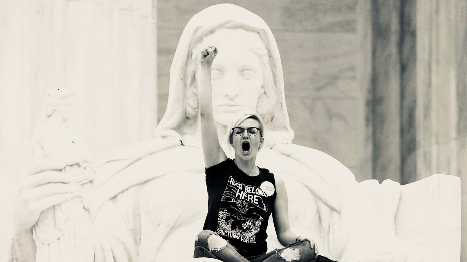 A protester sits on the lap of “Lady Justice” on the steps of the US Supreme Court.