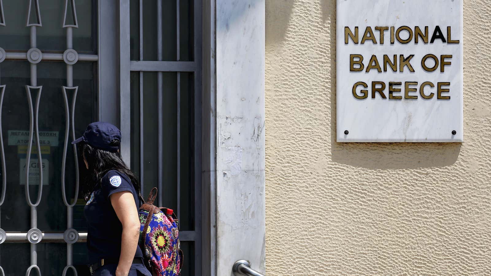 A coast guard officer looks through a locked gate at a National Bank of Greece branch in Piraeus.