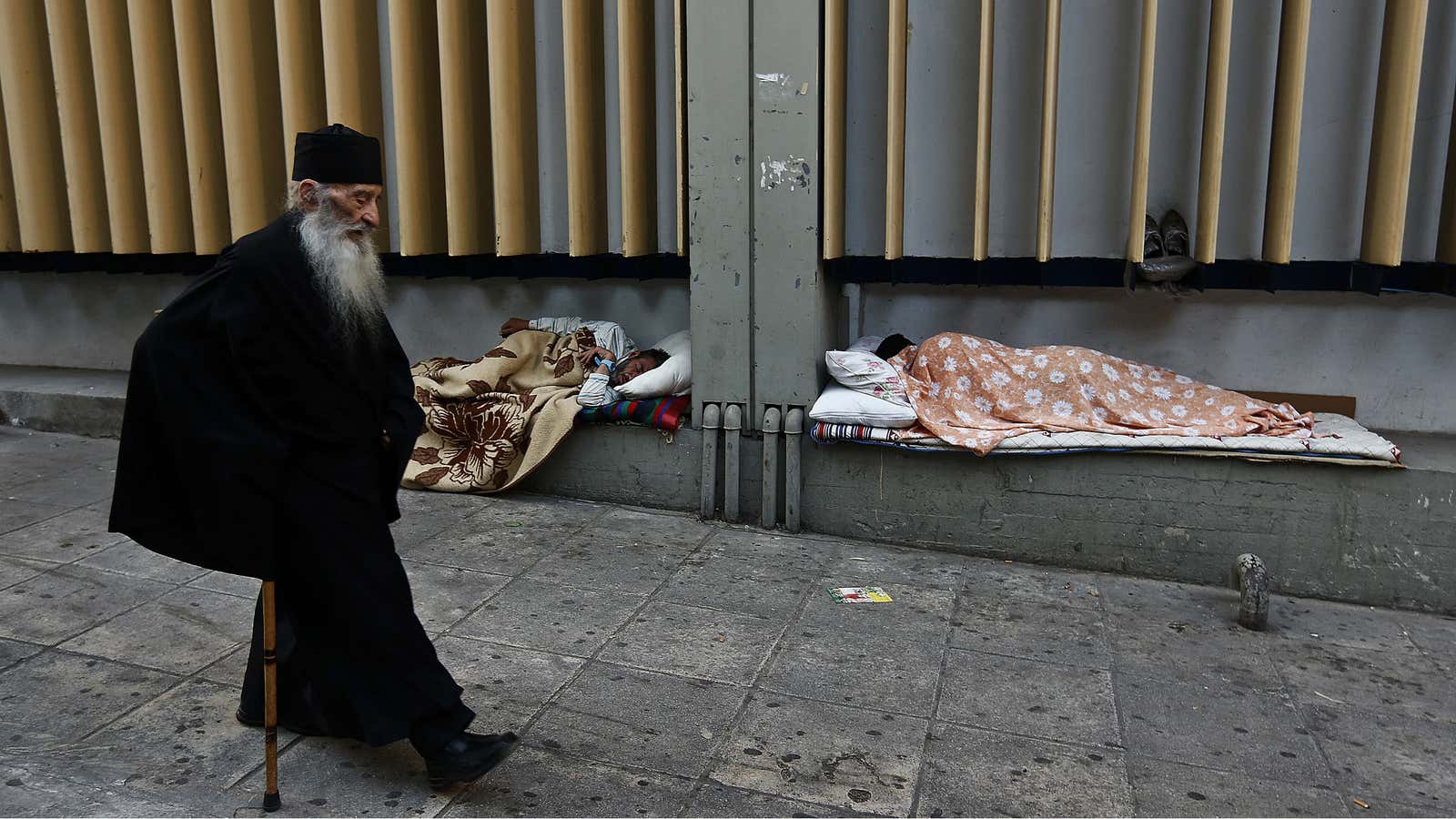 A monk passes homeless men in central Athens.